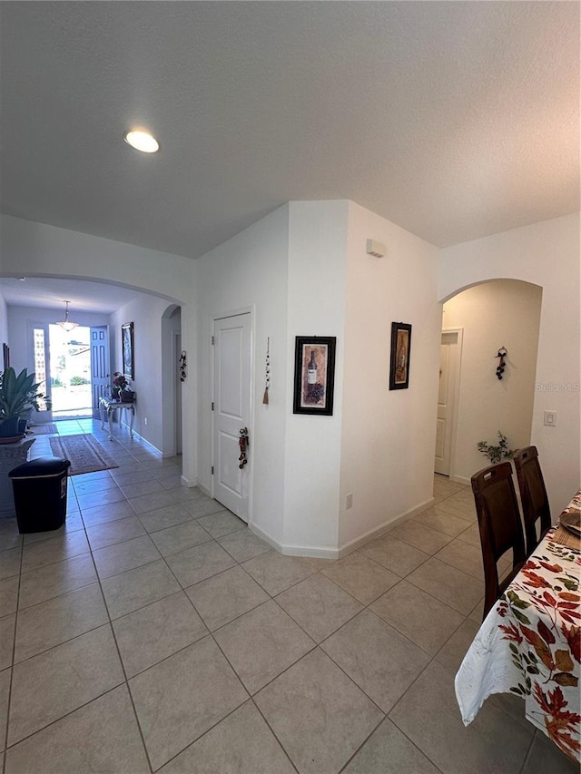 corridor with baseboards, arched walkways, a textured ceiling, and light tile patterned flooring