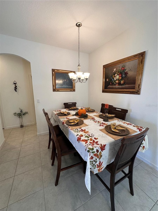 tiled dining space featuring arched walkways, a textured ceiling, baseboards, and a notable chandelier