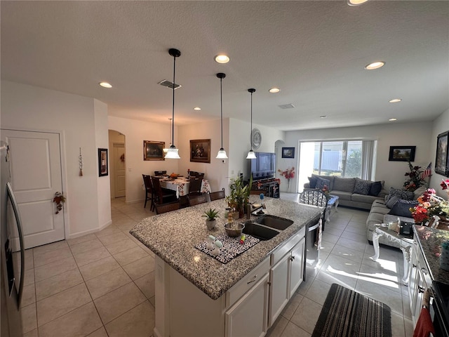 kitchen with arched walkways, open floor plan, white cabinets, a kitchen island, and a sink