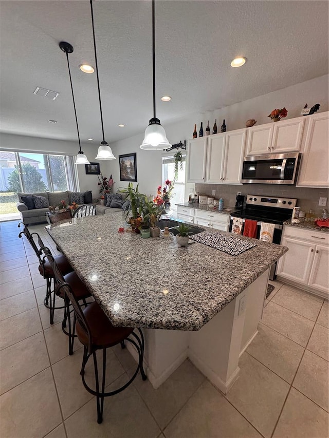 kitchen featuring stainless steel appliances, open floor plan, white cabinets, and hanging light fixtures