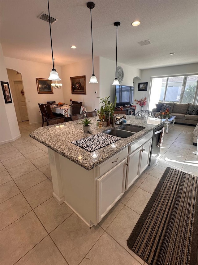 kitchen with a center island with sink, white cabinets, sink, light tile patterned flooring, and light stone counters