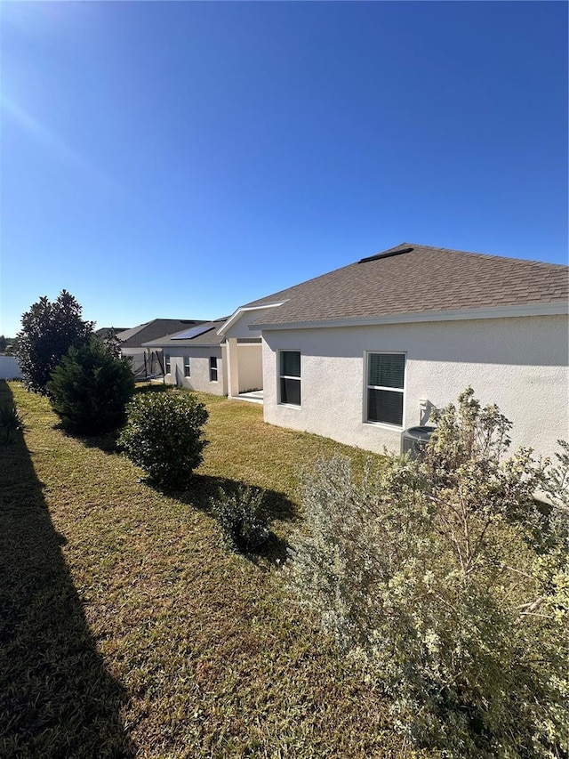 view of side of property with roof with shingles, a yard, and stucco siding