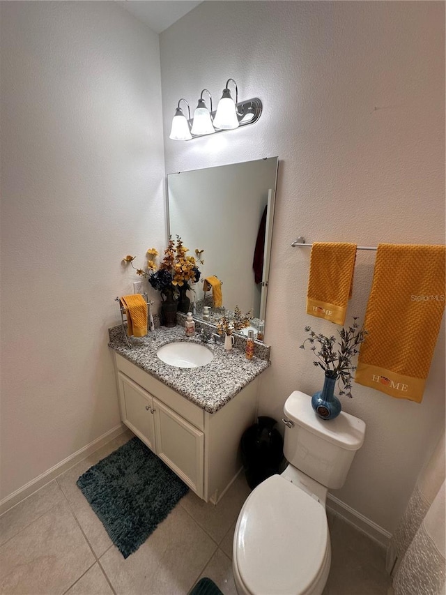 half bathroom with toilet, vanity, baseboards, and tile patterned floors