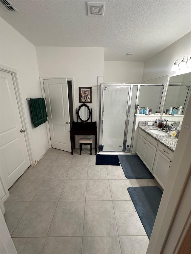 bathroom with a textured ceiling, vanity, tile patterned floors, and walk in shower