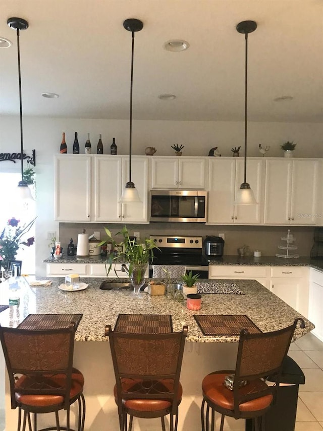 kitchen with appliances with stainless steel finishes, white cabinetry, hanging light fixtures, and a kitchen breakfast bar