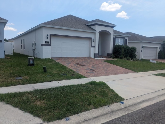 ranch-style home featuring a front lawn, decorative driveway, an attached garage, and stucco siding