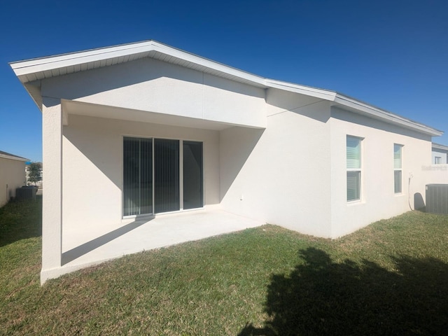 rear view of house featuring a yard, central air condition unit, a patio, and stucco siding