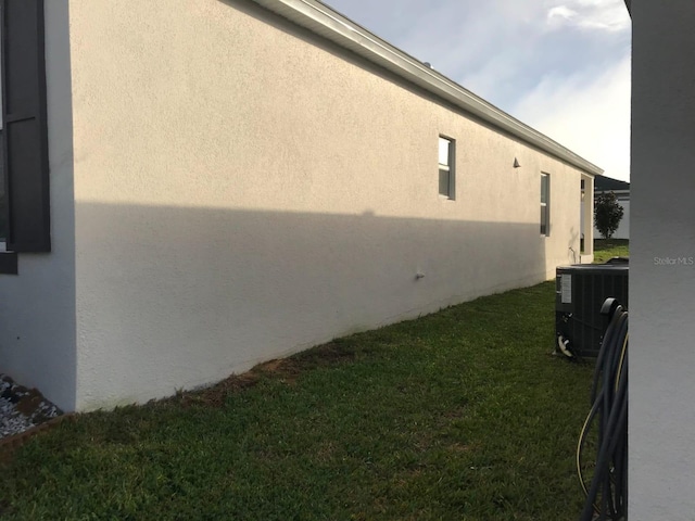 view of side of home with central AC, a yard, and stucco siding