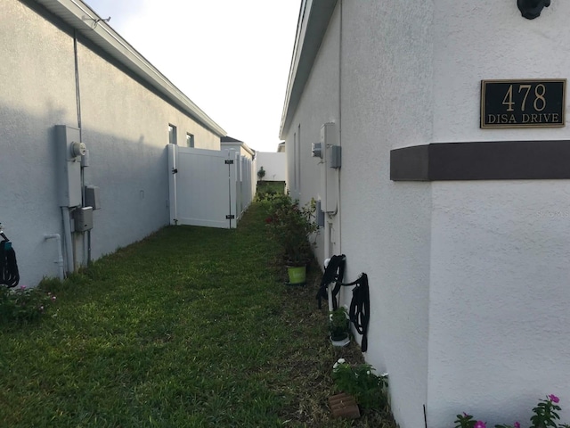 view of side of property with a gate, a lawn, and stucco siding