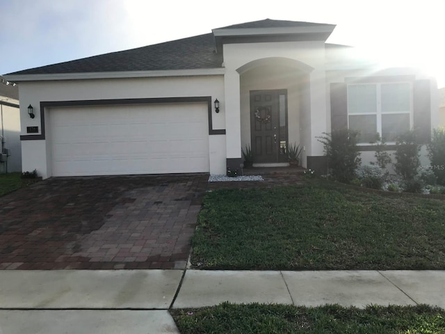 ranch-style home with a front lawn, decorative driveway, an attached garage, and stucco siding