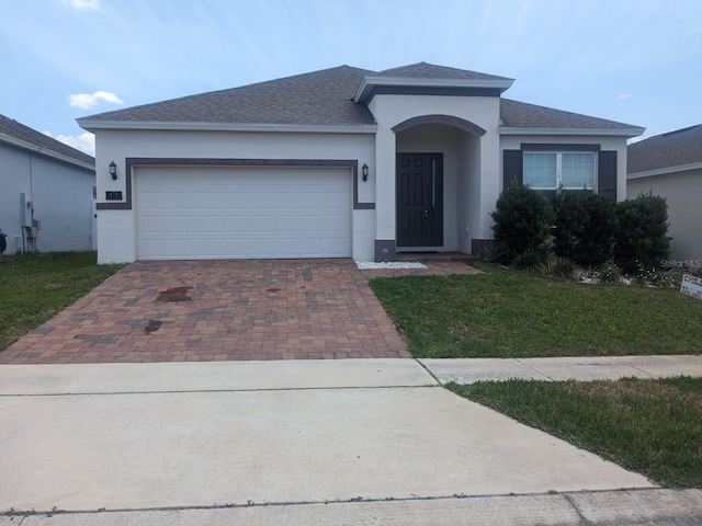 ranch-style house with a garage, roof with shingles, decorative driveway, stucco siding, and a front yard