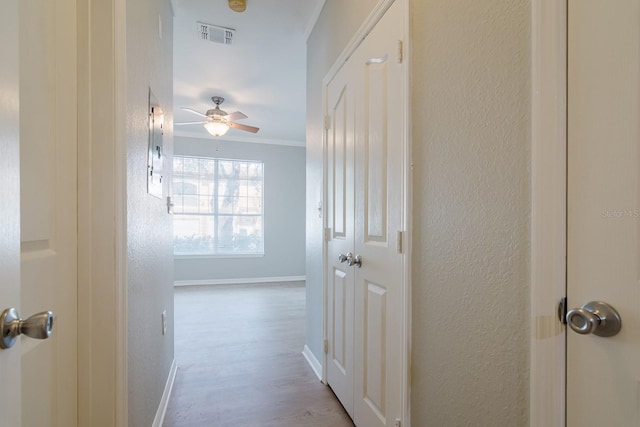 corridor featuring a textured wall, light wood finished floors, visible vents, and baseboards