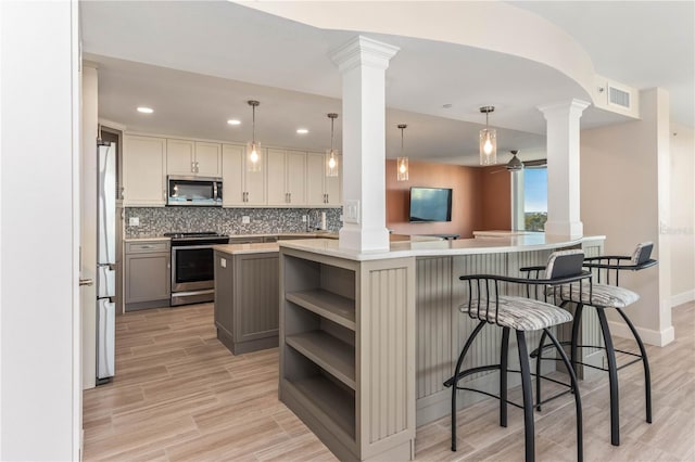 kitchen featuring ornate columns, decorative light fixtures, gray cabinets, kitchen peninsula, and stainless steel appliances