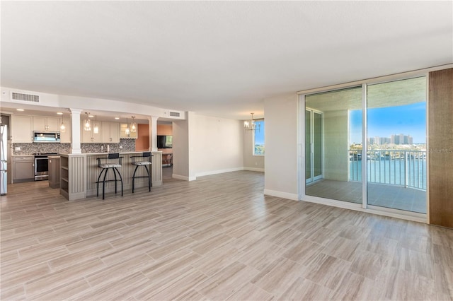 unfurnished living room with expansive windows, light hardwood / wood-style floors, a chandelier, and ornate columns