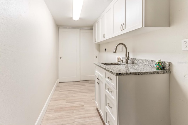 kitchen featuring white cabinetry, light stone countertops, sink, and light hardwood / wood-style floors