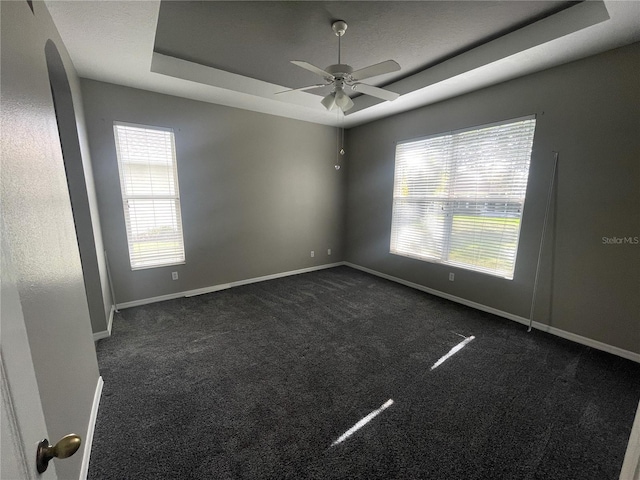 unfurnished room featuring a tray ceiling, ceiling fan, and dark carpet