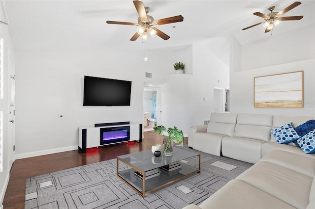 living room featuring ceiling fan, hardwood / wood-style floors, and a towering ceiling