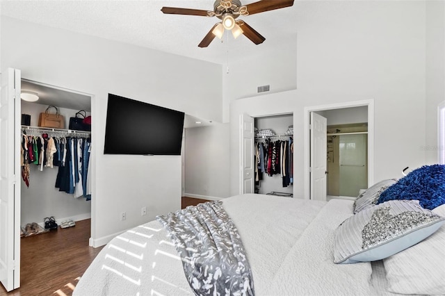 bedroom featuring two closets, ceiling fan, a towering ceiling, and dark hardwood / wood-style floors