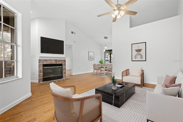 living room featuring a fireplace, high vaulted ceiling, light hardwood / wood-style flooring, and ceiling fan