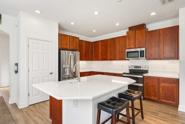 kitchen with sink, stainless steel appliances, a kitchen island with sink, and a breakfast bar area