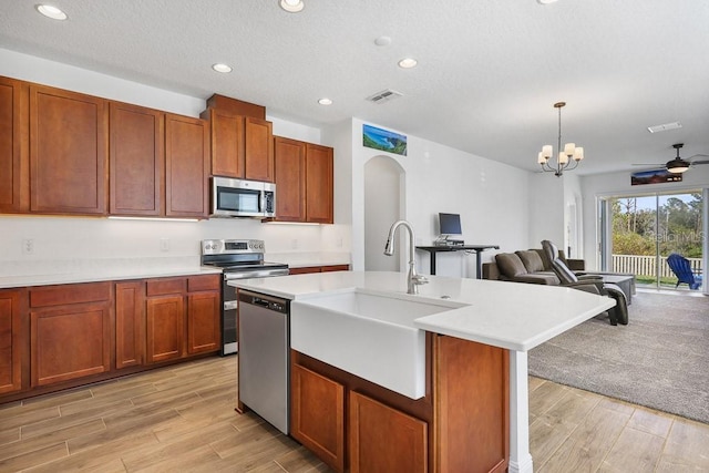 kitchen featuring sink, stainless steel appliances, decorative light fixtures, a center island with sink, and ceiling fan with notable chandelier