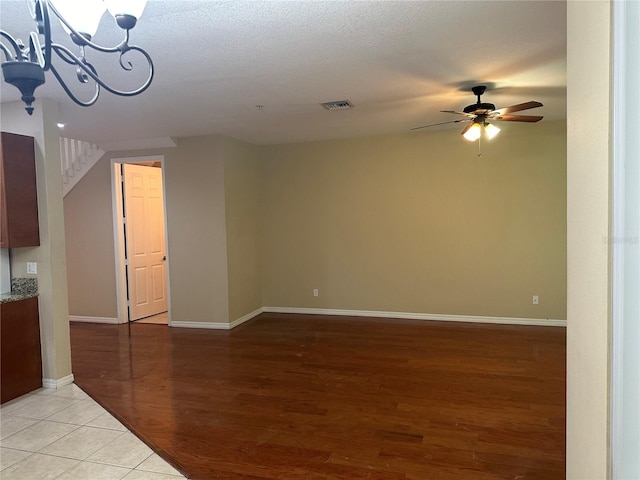 unfurnished living room featuring ceiling fan with notable chandelier, light hardwood / wood-style floors, and a textured ceiling