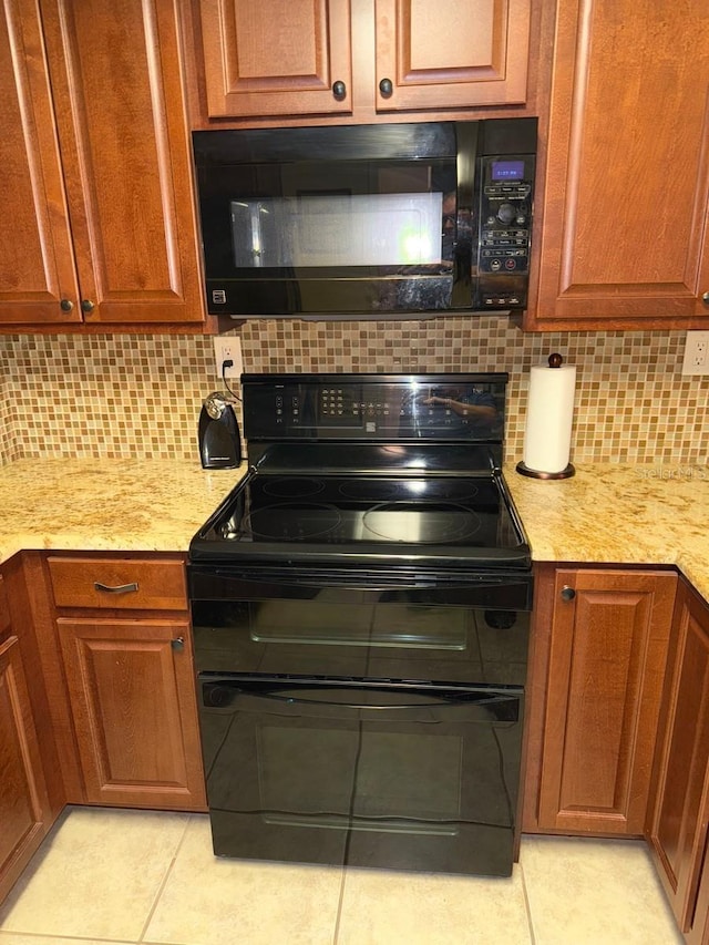 kitchen featuring tasteful backsplash, light stone countertops, light tile patterned floors, and black appliances