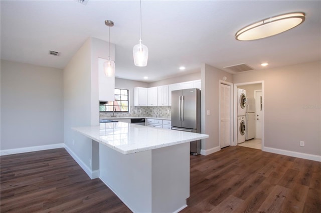 kitchen with kitchen peninsula, stainless steel appliances, stacked washer / dryer, white cabinetry, and hanging light fixtures