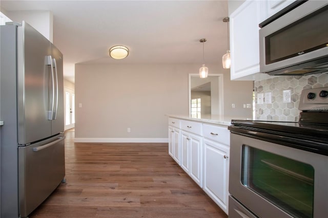 kitchen featuring tasteful backsplash, appliances with stainless steel finishes, decorative light fixtures, white cabinets, and hardwood / wood-style flooring