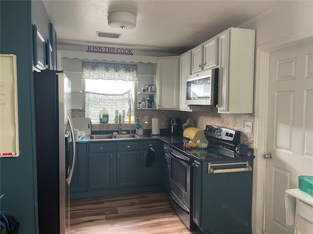 kitchen featuring hardwood / wood-style flooring, backsplash, stainless steel appliances, white cabinets, and a textured ceiling