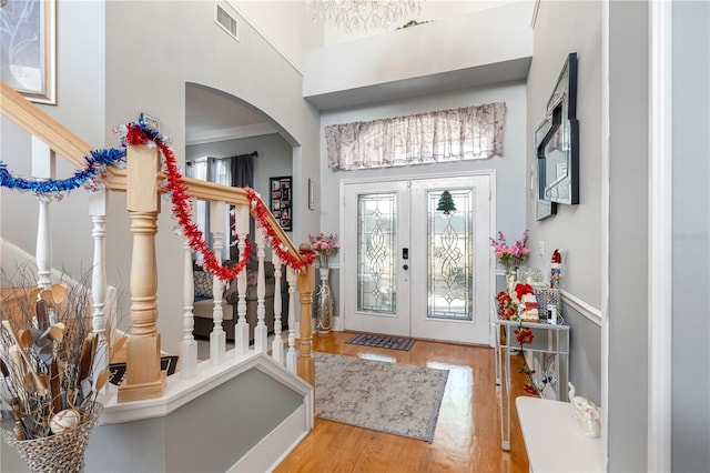 foyer entrance with hardwood / wood-style floors, a towering ceiling, and french doors