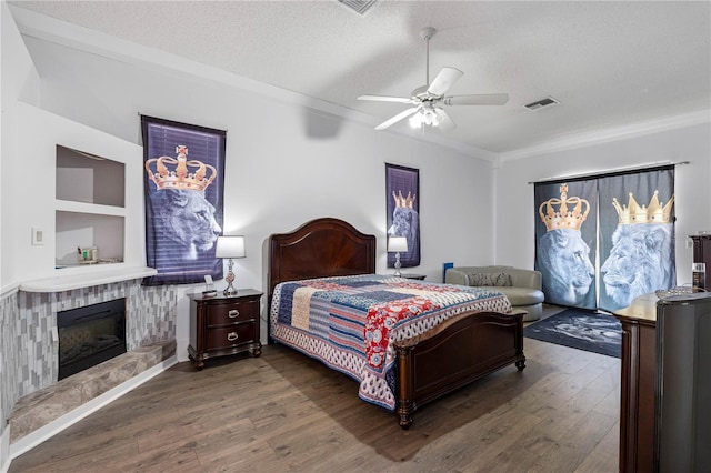 bedroom featuring dark hardwood / wood-style floors, a fireplace, ornamental molding, ceiling fan, and a textured ceiling