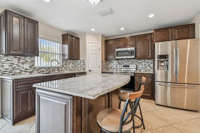 6213 Venezia Pl, Riverview, FL 33578 - kitchen featuring appliances with stainless steel finishes, a kitchen island, light tile patterned flooring, dark brown cabinetry, and tasteful backsplash