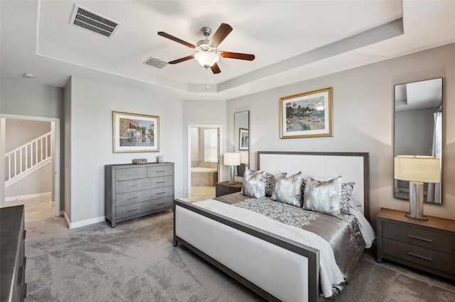 carpeted bedroom featuring ceiling fan, connected bathroom, and a tray ceiling