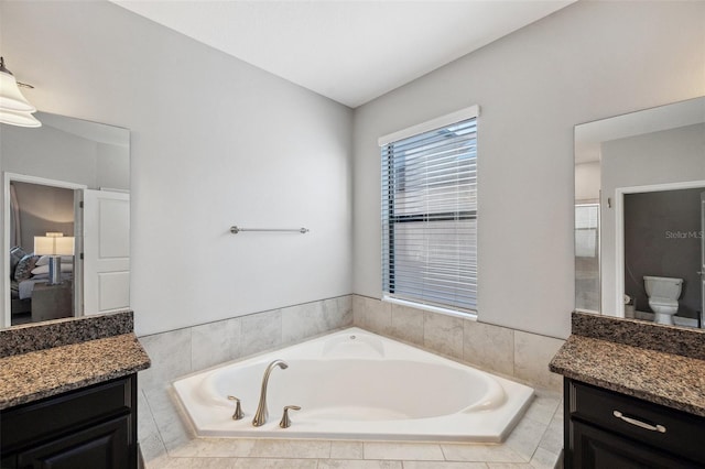 bathroom with tiled bath, vanity, and toilet