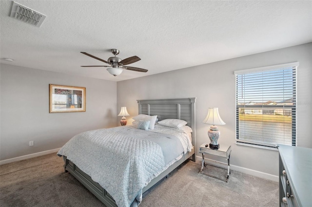 bedroom with ceiling fan, light colored carpet, and a textured ceiling