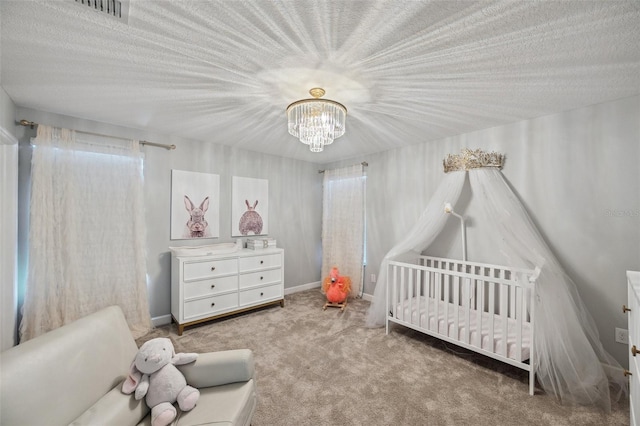 carpeted bedroom featuring a textured ceiling, an inviting chandelier, and a nursery area