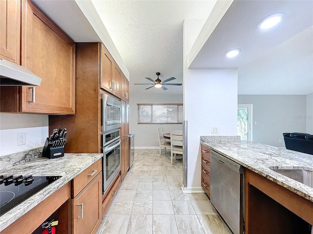 kitchen featuring a textured ceiling, ceiling fan, stainless steel appliances, and light stone counters