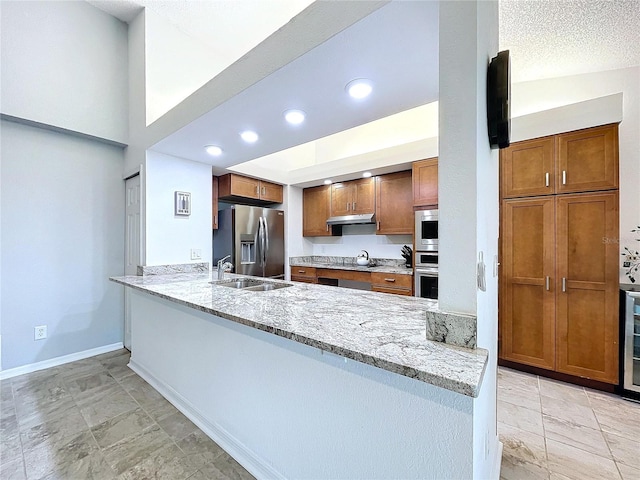 kitchen with light stone countertops, appliances with stainless steel finishes, kitchen peninsula, a textured ceiling, and sink