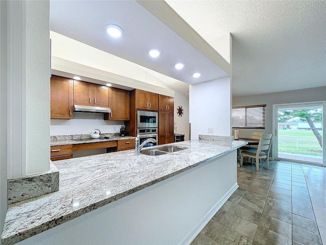 kitchen featuring sink, vaulted ceiling, light stone countertops, appliances with stainless steel finishes, and kitchen peninsula