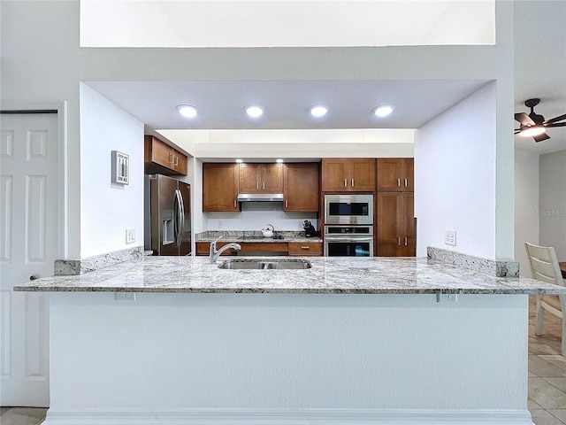 kitchen with kitchen peninsula, stainless steel appliances, light stone countertops, and sink