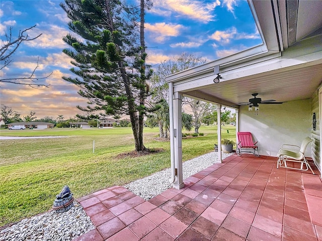 patio terrace at dusk with ceiling fan and a yard