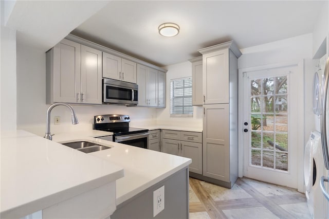 kitchen featuring kitchen peninsula, gray cabinets, sink, and appliances with stainless steel finishes