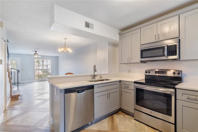 kitchen with kitchen peninsula, appliances with stainless steel finishes, gray cabinetry, ceiling fan with notable chandelier, and sink