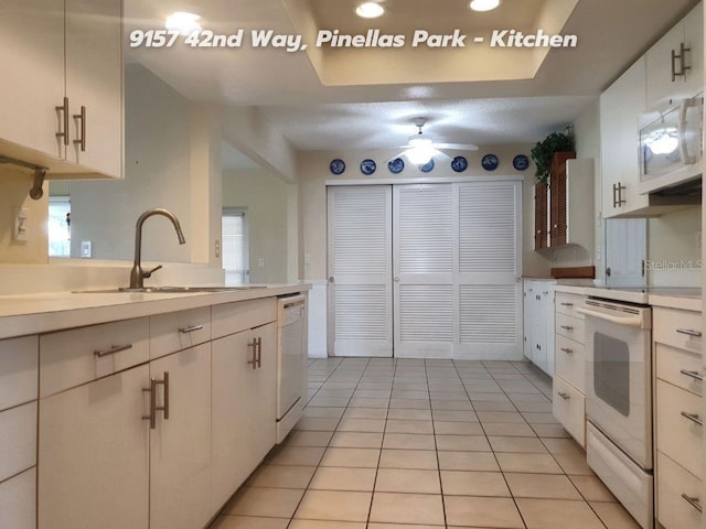 kitchen featuring sink, light tile patterned floors, dishwasher, white cabinetry, and a raised ceiling