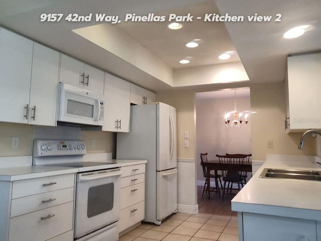 kitchen with sink, white appliances, white cabinetry, hanging light fixtures, and a raised ceiling