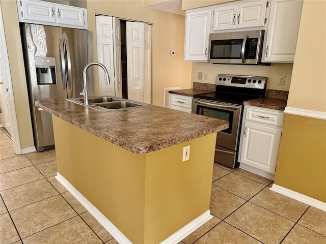 kitchen with a center island with sink, white cabinets, sink, light tile patterned floors, and appliances with stainless steel finishes