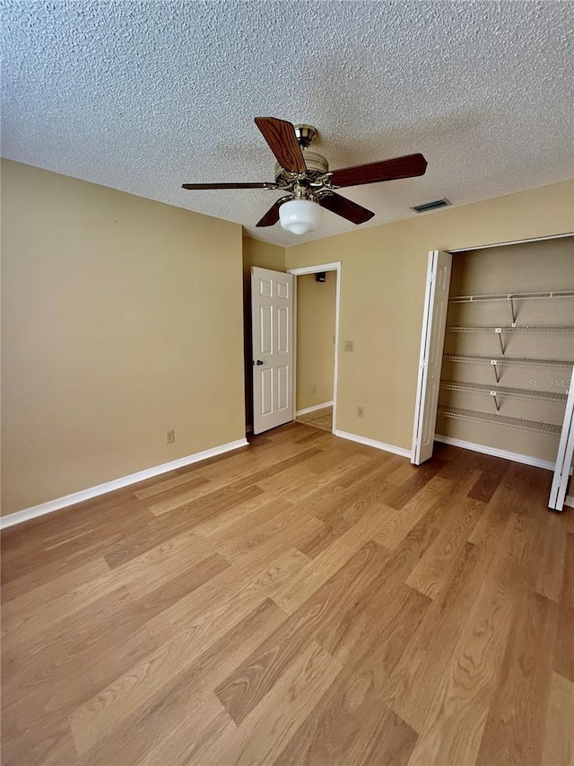 unfurnished bedroom with ceiling fan, a closet, a textured ceiling, and light hardwood / wood-style flooring