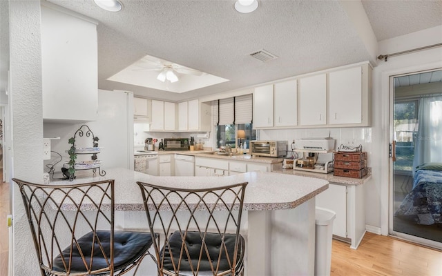 kitchen featuring a kitchen bar, white cabinetry, white appliances, and kitchen peninsula