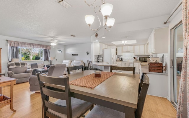 dining space with a textured ceiling, ceiling fan with notable chandelier, and light hardwood / wood-style floors